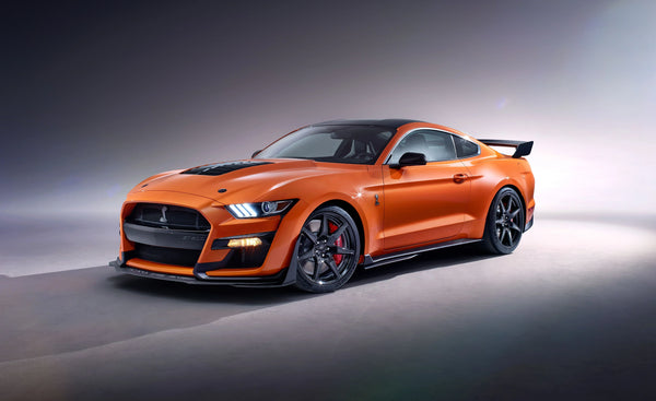 Orange 2020 Ford Mustang Shelby GT500 sports car with black hood and rear spoiler on studio floor