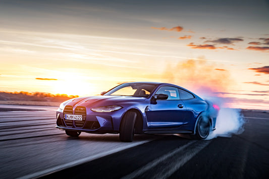 Blue BMW M4 sports car drifting on asphalt road at sunset with smoke from rear tires