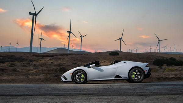 White Lamborghini Huracan Evo RWD Spyder parked on road with wind turbines and sunset in background