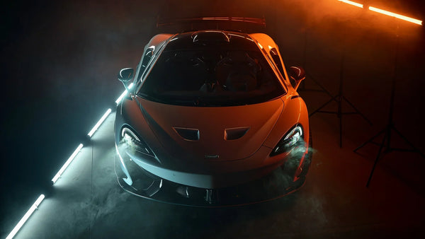 Front view of silver McLaren sports car with illuminated headlights in dark studio with fog and colored lights