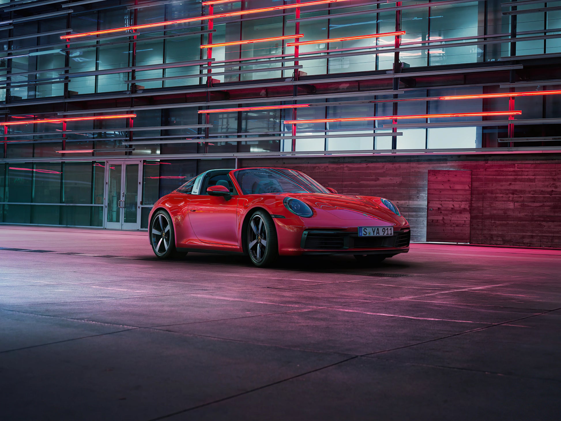 Red Porsche 911 Targa 4S sports car parked in modern urban setting with glass and neon lights