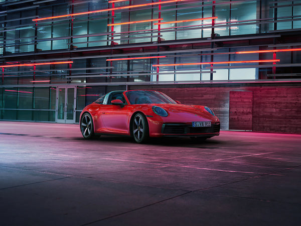 Red Porsche 911 Targa 4S sports car parked in modern urban setting with glass and neon lights