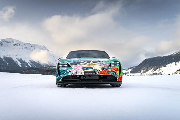 Front view of a Porsche Taycan 4S electric car with colorful floral art wrap on snowy mountain landscape