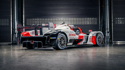 2021 Toyota GR010 Hybrid race car in white, red, and black inside garage with metal roller doors