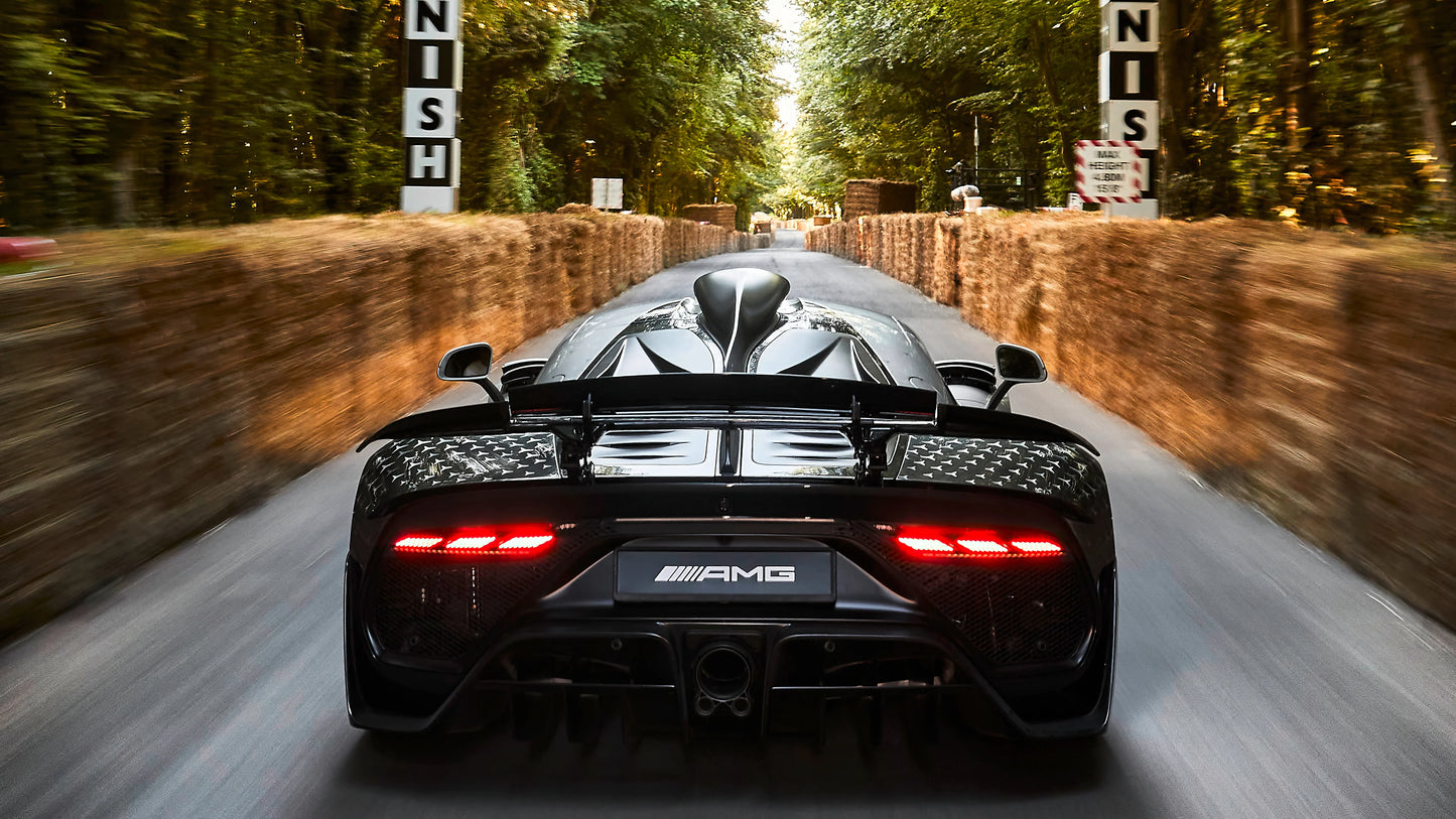 Rear view of black 2022 Mercedes AMG One hypercar speeding on forest road with hay bale barriers