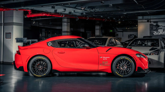 Red Toyota GR Supra GT4 50 Edition race car in indoor garage with black wheels and Pirelli tires
