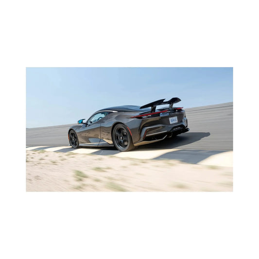 Black sports car with rear spoiler driving on banked race track under clear blue sky