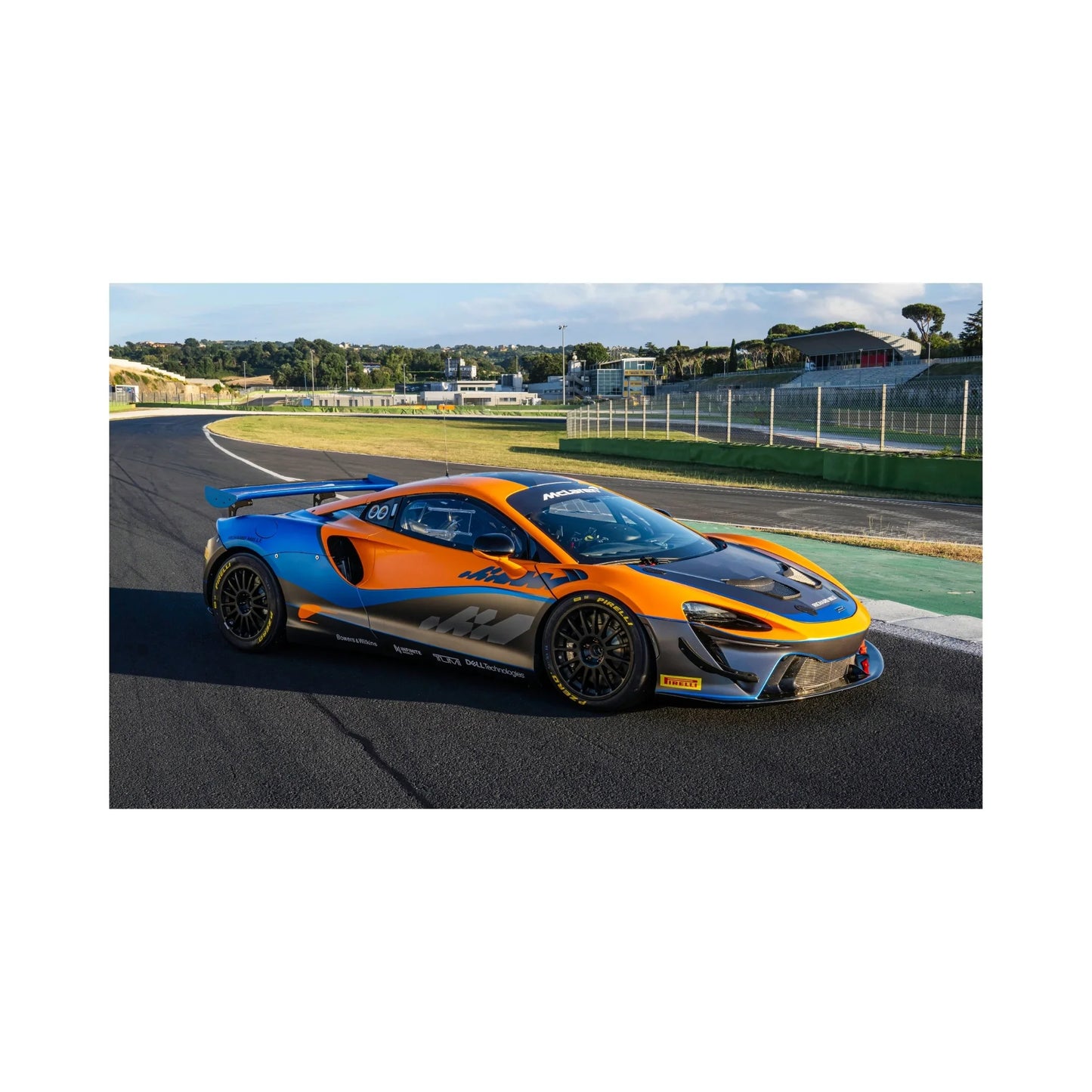 Orange and blue McLaren race car on a racetrack with grandstands and clear sky