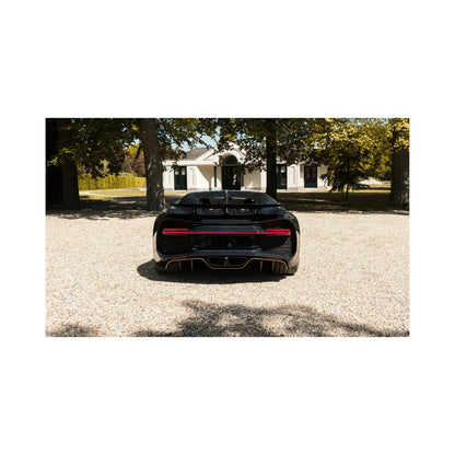 Rear view of a black luxury sports car on gravel driveway with a large white house and trees in background