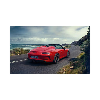 Red Porsche 911 convertible driving on a coastal road with ocean and hills in the background