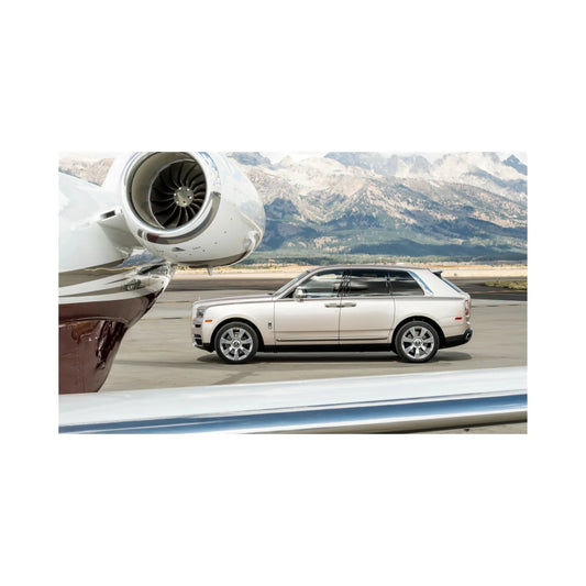 Silver Rolls-Royce SUV parked near a private jet engine on runway with mountain backdrop