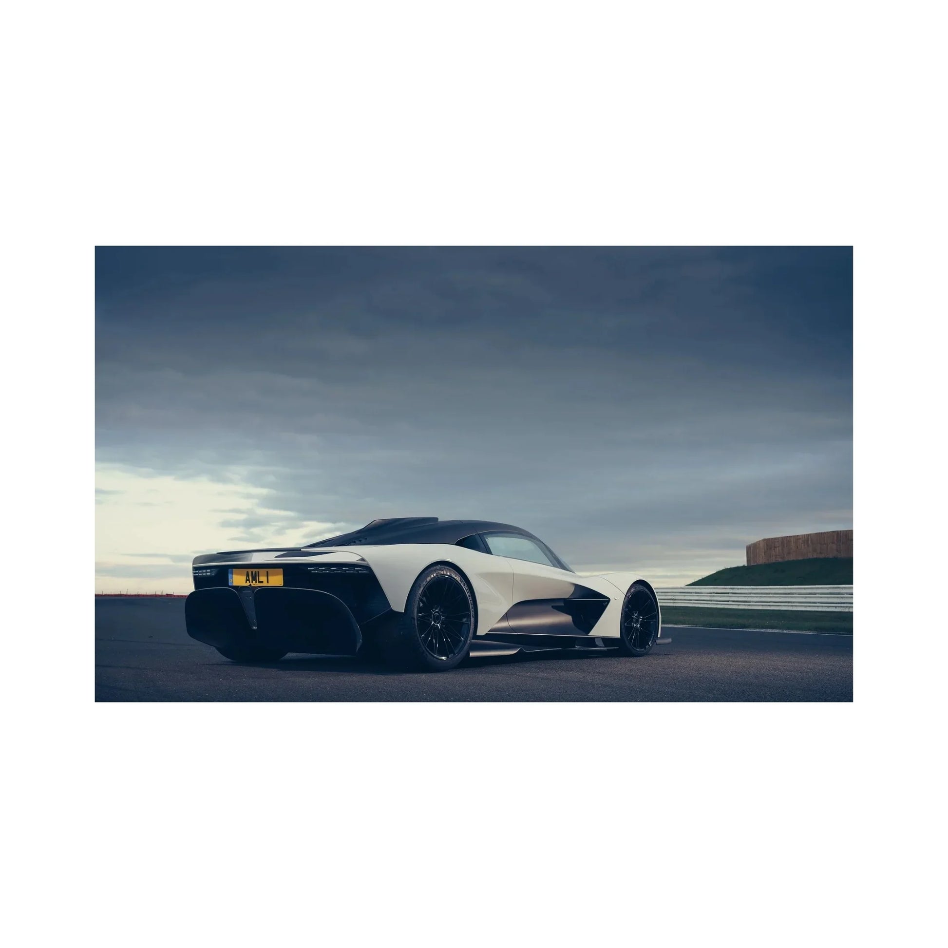 Rear side view of a white and black luxury sports car on a racetrack under a cloudy sky
