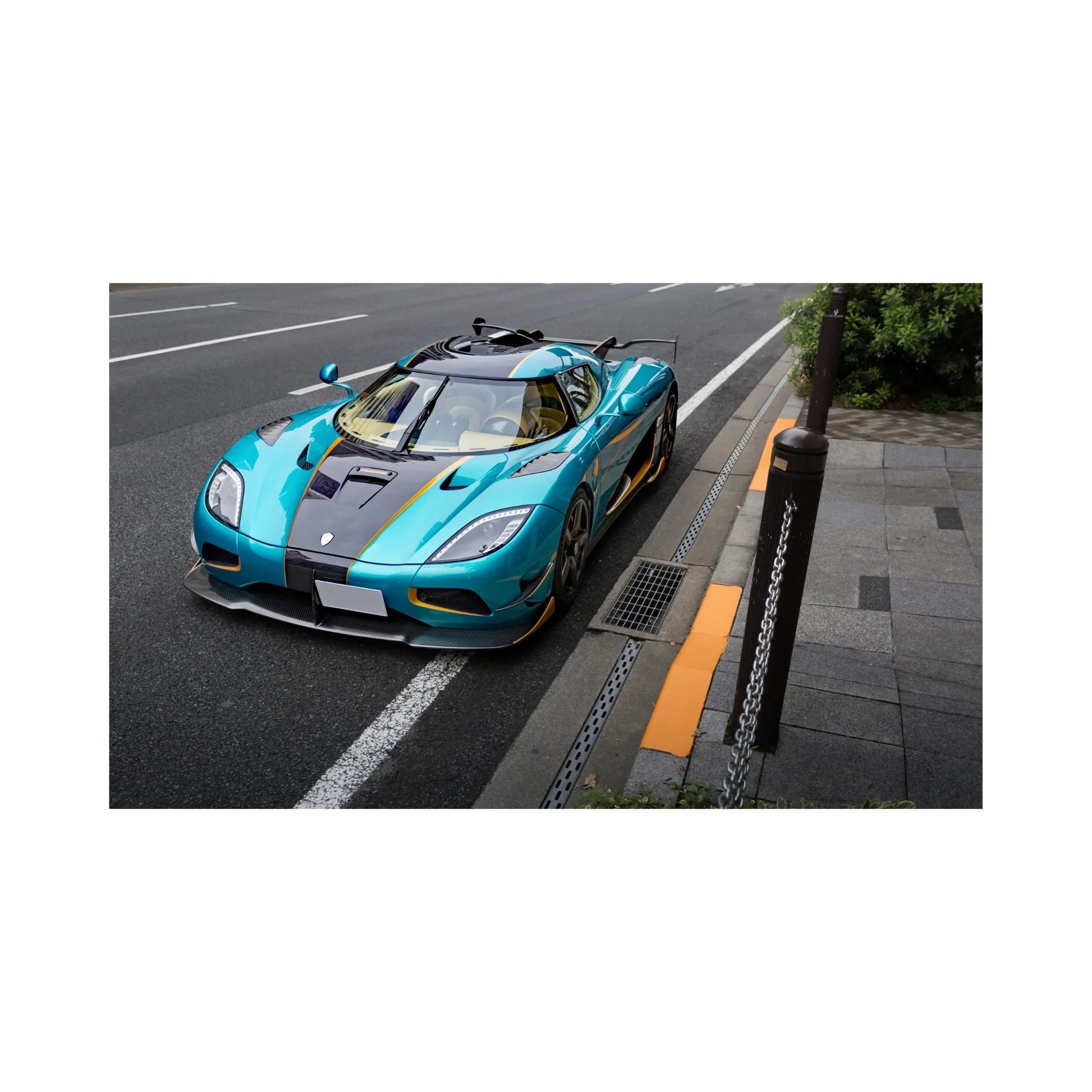 Luxury teal and black Koenigsegg supercar parked on city street near sidewalk with chain posts