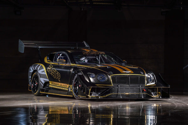 Black and gold Bentley Continental GT3 race car with large rear wing in dark indoor setting